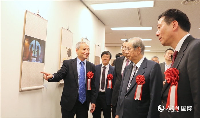 “湖州印象”攝影展主創(chuàng)、世界華人攝影協(xié)會副會長馮學(xué)敏向吳江浩大使、福田康夫前首相等嘉賓介紹展出作品。（人民網(wǎng) 許可攝）