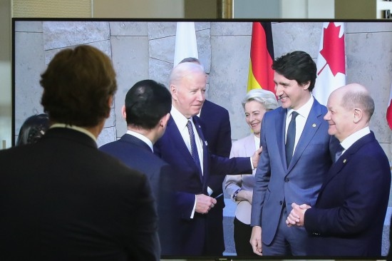 2022年3月24日，在比利時(shí)布魯塞爾的北約總部，一名男子觀看屏幕上美國(guó)總統(tǒng)拜登（右四）、歐盟委員會(huì)主席馮德萊恩（右三）、加拿大總理特魯多（右二）、德國(guó)總理朔爾茨（右一）出席七國(guó)集團(tuán)峰會(huì)合影儀式的畫(huà)面。新華社記者鄭煥松攝