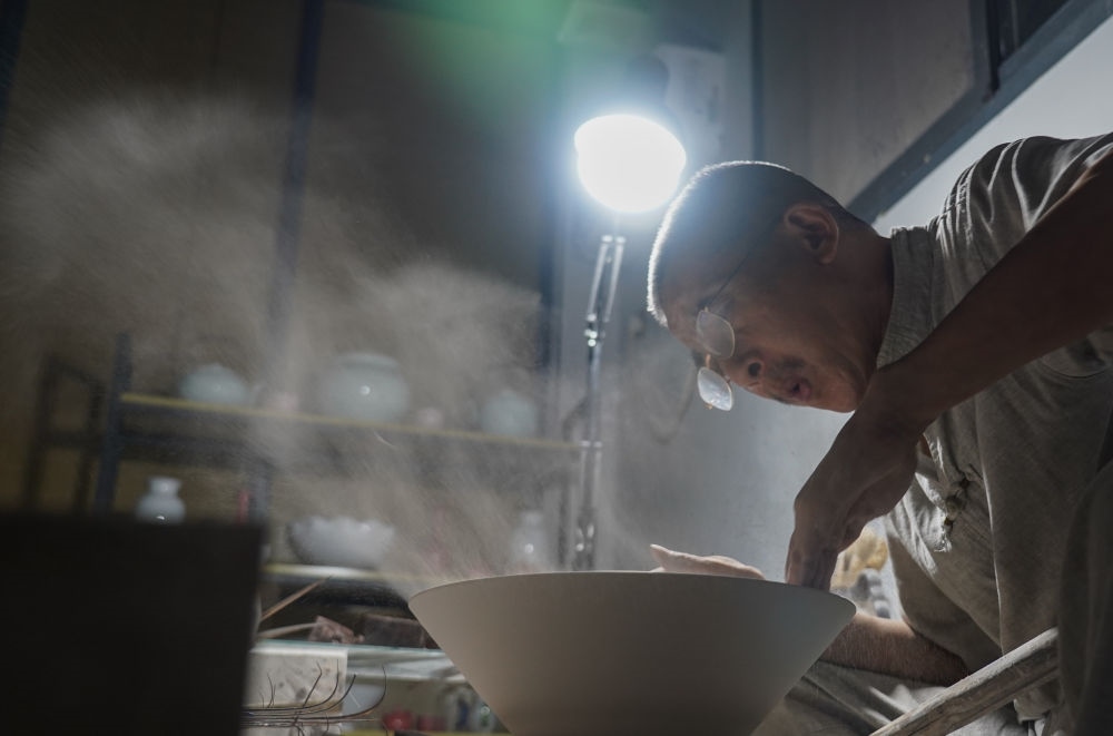 ↑ 在景德鎮(zhèn)，手工匠人吹去坯內(nèi)的泥土（2021年7月14日攝）。