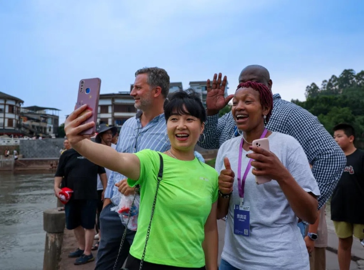 2024“一帶一路”媒體合作論壇聯(lián)合采訪調(diào)研行成員在樂山蘇稽古鎮(zhèn)與游客合影留念。本報(bào)記者 伊霄攝