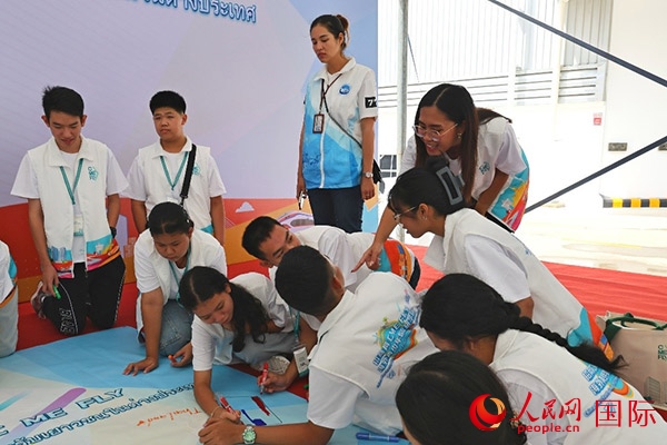 泰國學(xué)生在開營儀式展板上繪制圖案。人民網(wǎng)記者 白元琪攝