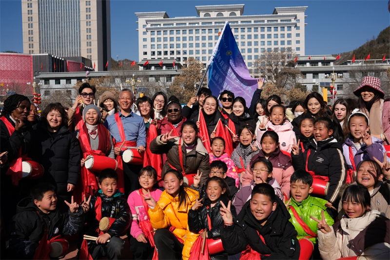 中外青年學子在安塞文化廣場觀看陜北腰鼓和大秧歌表演后合影留念，大家踏著鼓點共舞，翻飛的紅綢與躍動的身影交織，在黃土地廣場上繪出一幅生動的陜北民俗互動畫卷